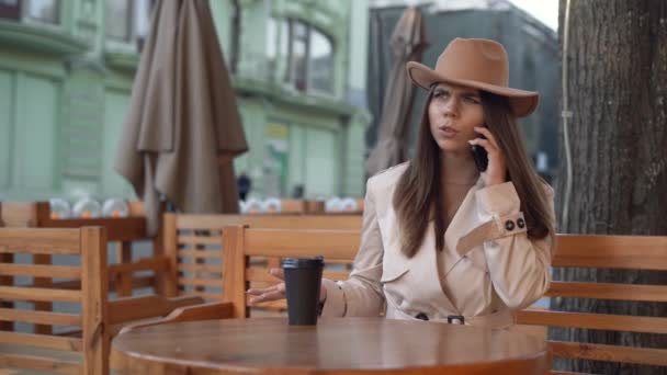 Młoda piękna Europejka siedzi przy stole w kawiarni na ulicy. zły nastrój, rozmowa przez telefon — Wideo stockowe