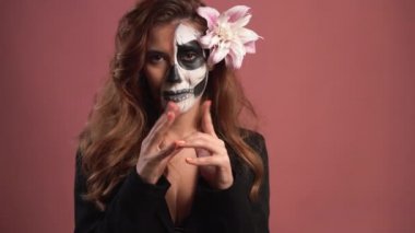 Pembe arka planda Cadılar Bayramı için makyaj yapmış genç bir kadının portresi. yüzün önünde parmak hareketi