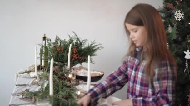 Küçük kız, şenlikli bir Noel yemeği için masayı dekore etmeye yardım ediyor. peçete koyar. — Stok video