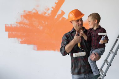 Mutlu genç aile evlerini yeniliyor, baba oğlunu kollarında tutuyor. Parmağını kaldır..