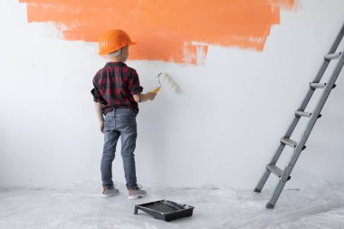 Koruyucu turuncu şapkalı çocuk duvarı boyuyor..