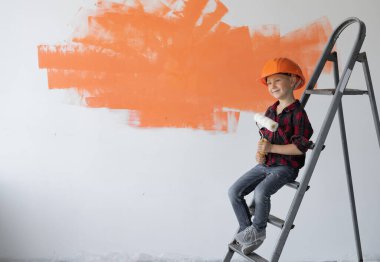 Koruyucu turuncu giysili çocuk inşaat merdiveninde oturuyor..