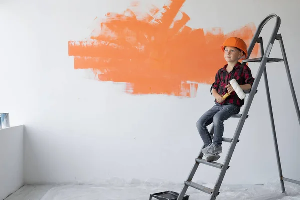 Niño vestido de naranja protectora se sienta en una escalera de construcción. Copiar espacio. — Foto de Stock