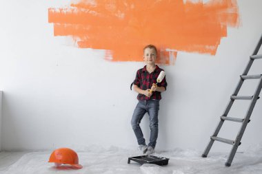 Bir çocuk elinde boya silindiri tutarken yanında duruyor. Ev yenileme konsepti.