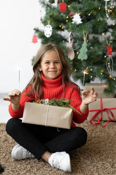 En flicka med europeiskt utseende sitter nära julgranen. — Stockfoto