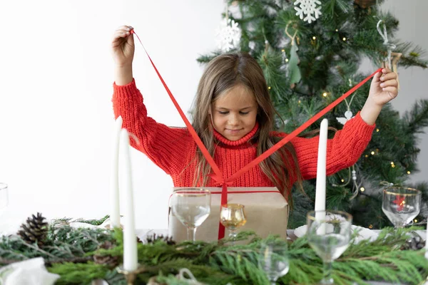 Noel ağacının yanında duran küçük bir kız hediyeli bir kutuyu açıyor.. — Stok fotoğraf