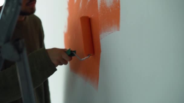 一个男人的手的特写。用滚筒在墙上涂上橙色的油漆. — 图库视频影像