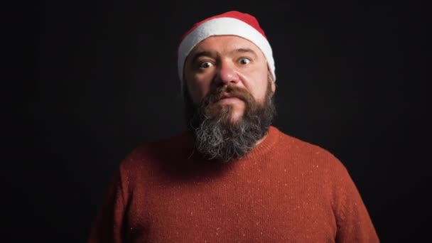 Noel Baba şapkası takmış iyi beslenmiş sakallı bir adam iki palmiyeyle sevinir, yüzünü kapatır. Siyah arka plan. Noel konsepti — Stok video