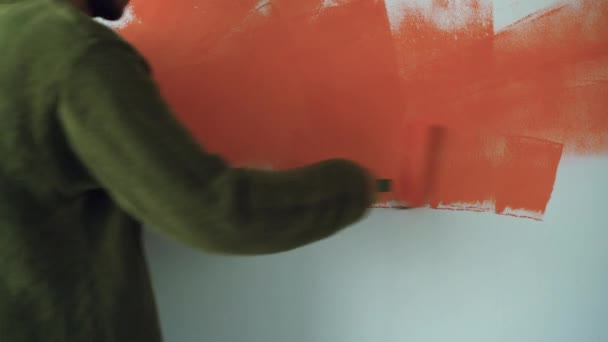 Um homem está perto da parede e pinta com um rolo laranja. Espaço para cópia. Conceito de renovação de casa — Vídeo de Stock