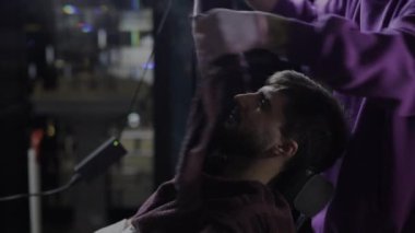 Kuaför tıraş olmadan önce genç sakallı adamın yüzünü sıcak havluyla örter.