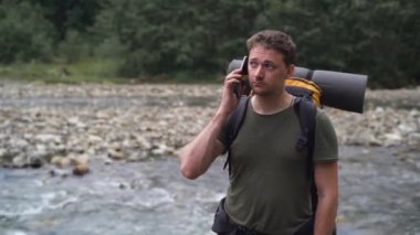 Sırt çantalı bir turist nehir kenarında duruyor ve telefonda mesaj yazıyor.