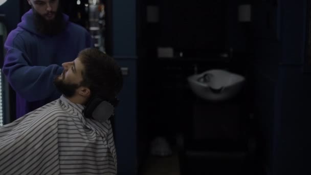 Een man met een baard knipt zijn baard in een kapperszaak. Man kapper borstels haar van klanten gezicht — Stockvideo
