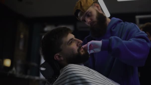 Un barbudo se corta la barba en una peluquería. Hombre peluquero peinando cabello y cortando con tijeras — Vídeo de stock