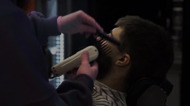 Un barbudo se corta la barba en una peluquería. Peluquero alisa el cabello y corta con un trimer — Vídeo de stock