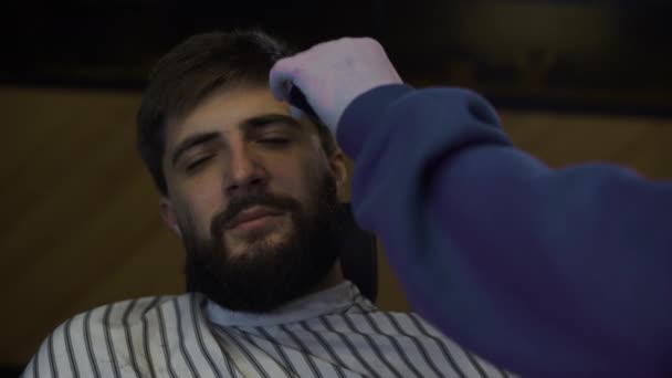 Un barbudo se corta la barba en una peluquería. Hombre peluquero peinando el cabello y corte con un trimer — Vídeos de Stock