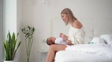 Genç ve güzel bir kadın yatakta oturur, emziren yeni doğmuş bir bebek bacaklarının üzerinde yatar. Boşluğu kopyala