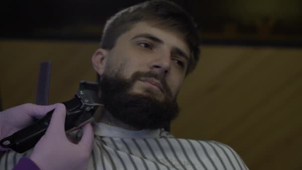 Бородатый мужчина в парикмахерской, парикмахер с триммером делает коррекцию бороды — стоковое видео