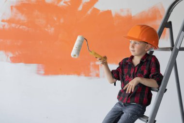 Koruyucu turuncu giysili bir çocuk inşaat merdiveni ucuna oturur ve silindirle boş bir yere mesaj için gider..
