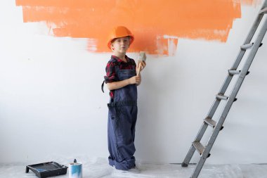 Tulum giymiş ve koruyucu kasklı bir çocuk duvarın yanında duruyor. Ev yenileme konsepti.