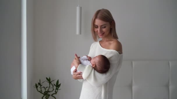 Fiatal, gyönyörű nő áll a szobában egy szoptató csecsemőt tartva a karjaiban. Boldog anyaság koncepciója — Stock videók