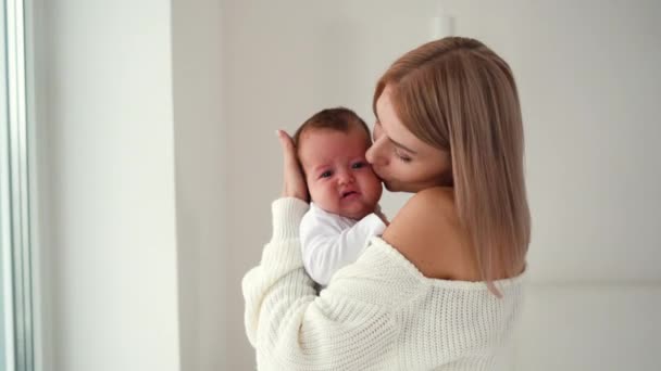 Fiatal gyönyörű nő tart egy újszülött a karjaiban sétál a szobában ölelések és csókok — Stock videók