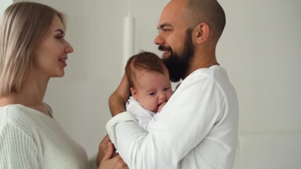 Ung kärleksfull kaukasiska familj med ett nyfött barn i rummet. Hemkläder och en mysig atmosfär. Brunett kvinna, skäggig man — Stockvideo