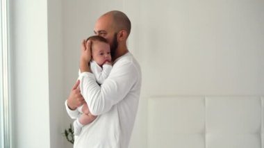 Mutlu bir adam odada duruyor kucağında yeni doğmuş bir bebeği tutuyor ve ona sarılıyor. Mutlu aile kavramı