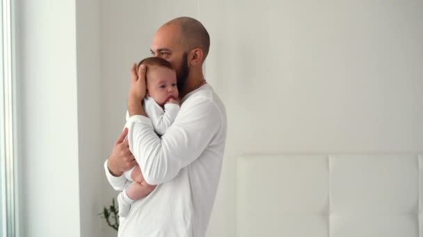 Egy boldog férfi áll a szobában egy újszülöttet tartva a karjaiban és megöleli. Boldog szülők koncepciója — Stock videók