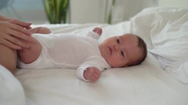 Yeni doğmuş bir bebek yatakta yatar ve gülümser, bir kadın elini karnına koyar. Anne yanağından öpüyor. Mutlu aile kavramı