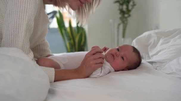 Egy újszülött fekszik az ágyon és mosolyog, egy nő megsimogatja a hasát. Anya kezet csókol. Boldog szülők koncepciója — Stock videók