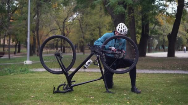 Un hombre en el parque arregla su bicicleta. Lo puso de cabeza. Concepto de renovación — Vídeos de Stock