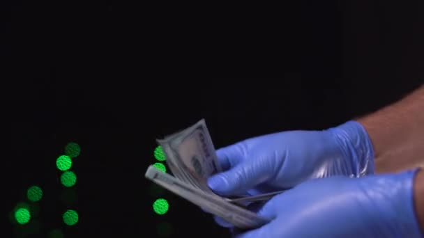 Męskie ręce w rękawiczkach medycznych liczą pieniądze na tle lampek świątecznych. Banknoty 100 dolarów — Wideo stockowe