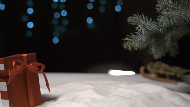 Sobre el fondo navideño una mano hembra deposita una caja empacada en papel artesanal. Copiar espacio — Vídeo de stock