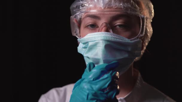 Giovane medico donna stanca indossa un cappotto bianco e occhiali di sicurezza. toglie la maschera protettiva dal viso e sospira pesantemente. Il concetto di lotta contro la covid-19 — Video Stock