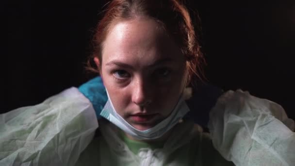 Μια νεαρή γυναίκα γιατρός φοράει μια προστατευτική άσπρη στολή και μια ιατρική μάσκα. έννοια της καταπολέμησης του coronavirus — Αρχείο Βίντεο