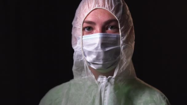 白い防護服を着た若い女性医師の肖像写真です。顔から医療マスクを削除します。covid-19と戦うという概念 — ストック動画