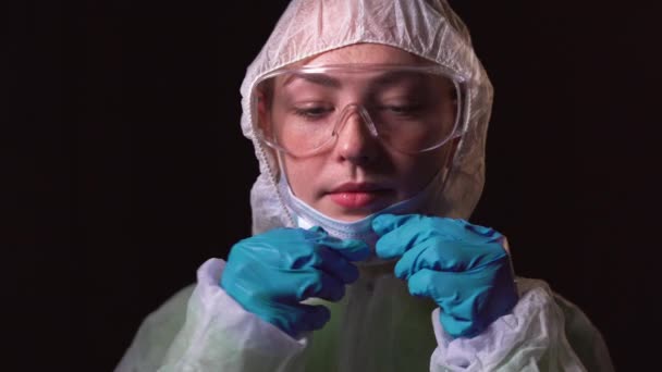흰 보호 복을 입은 젊은 여성 의사의 사진. 얼굴에 의료용 마스크를 씌웁니다. 공조 -19 와의 싸움의 개념 — 비디오
