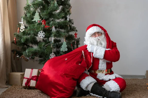 Noel Baba, Noel ağacının yanında yerde oturur çantayı çözer ve hediyesini çıkarır. — Stok fotoğraf
