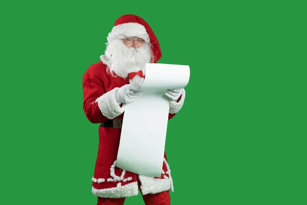 Weihnachtsmann auf grünem Grund hält eine Liste von Kindern in der Hand, die sie sorgfältig lesen. Überraschtes Gesicht. Kopierraum. — Stockfoto