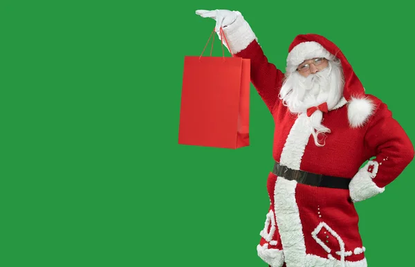 Santa claus sobre un fondo verde sostiene una bolsa de compras roja lo levanta. Copiar espacio. — Foto de Stock