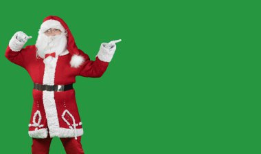 Yeşil arkaplandaki Noel Baba, metin için iki işaret parmağıyla boş bir yeri işaret ediyor. Boşluğu kopyala.