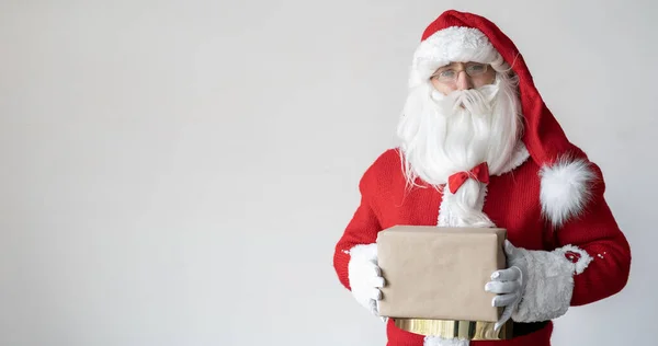 Święty Mikołaj trzyma prezent w papierowym pudełku przed sobą. Stoi w pobliżu miejsca na tekst. — Zdjęcie stockowe