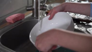 Bir kadının yakın çekimi, akan suyun altında büyük bir tabak verir..