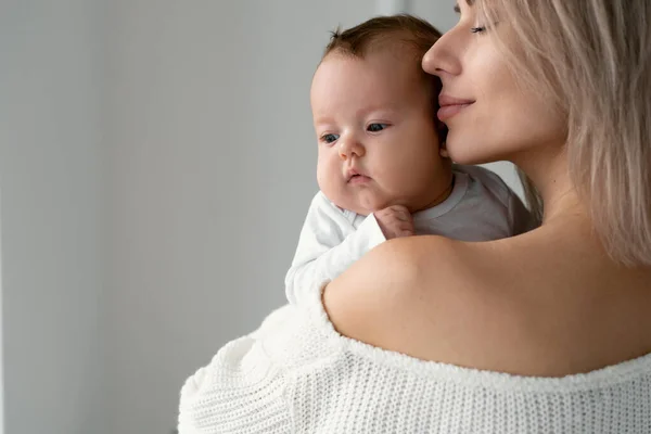 Mamá feliz sostiene a un bebé recién nacido en sus brazos y lo abraza. Trae sus labios a su mejilla. — Foto de Stock