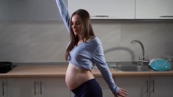 Беременная женщина танцует на кухне. Смешные движения рук и отличное настроение. Копирование пространства. — стоковое видео