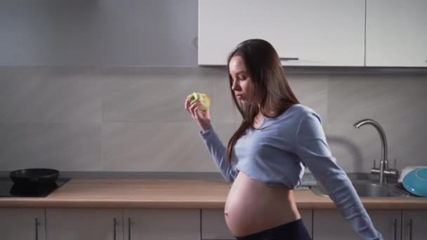 Mulher grávida dançando na cozinha. comer uma maçã verde Movimentos de mão engraçados e ótimo humor. Espaço de cópia. — Vídeo de Stock