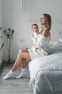 Güzel, genç bir anne ve kızı kollarında. Mutlu aile kavramı, annelik. Anne yatak odasında bebeğiyle oynuyor..