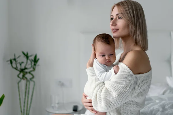 Una madre joven sostiene a un bebé recién nacido en sus brazos. Mujer y bebé en el dormitorio sobre un fondo blanco. Maternidad y concepto infantil. — Foto de Stock
