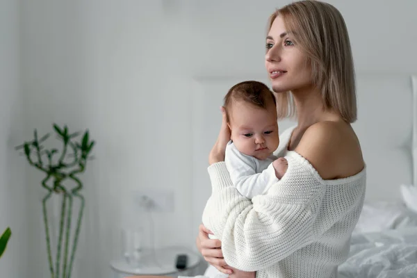 Genç bir anne yeni doğmuş bir bebeği kollarında tutuyor. Kadın ve bebek beyaz arka planda yatak odasında. Annelik ve çocukluk kavramı.