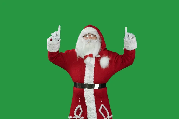 Weihnachtsmann auf grünem Hintergrund zeigt mit zwei Zeigefingern nach oben auf einen leeren Raum für den Text. Kopierraum. — Stockfoto